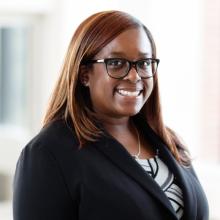 Tiarra Thomas wearing a blazer and glasses smiles at the camera