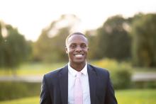 Kevin Russell standing wearing a dark suit and pink tie