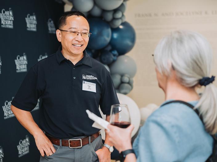 Two alumni chat in front of a backdrop of CWRU logos, and blue and silver balloons.