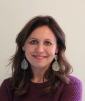 Headshot of smiling woman with long brown hair, purple sweater, and large silver earrings
