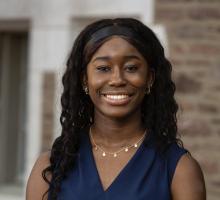 color outdoor image of smiling African American woman with long hair, wearing a navy blue sleeveless top and gold necklace