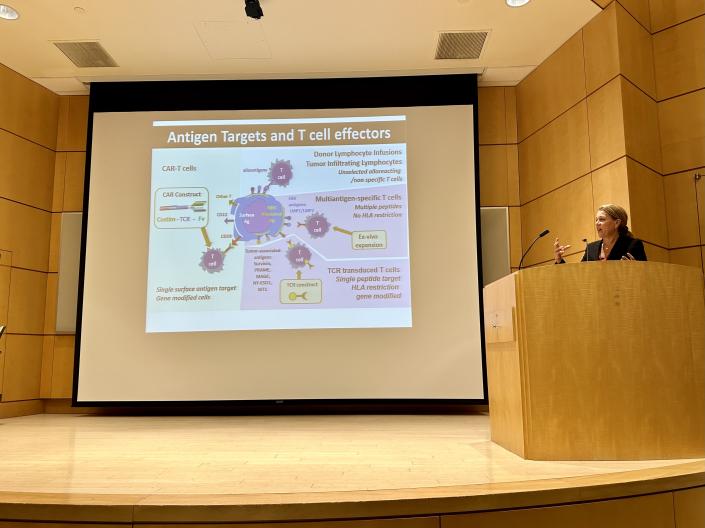 Catherine Bollard presenting behind a podium with a powerpoint at Seminar Series in the WRB aduitorium