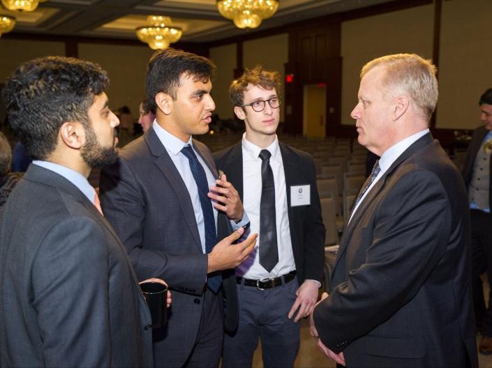 Four men in business attire talk in a conference hall.