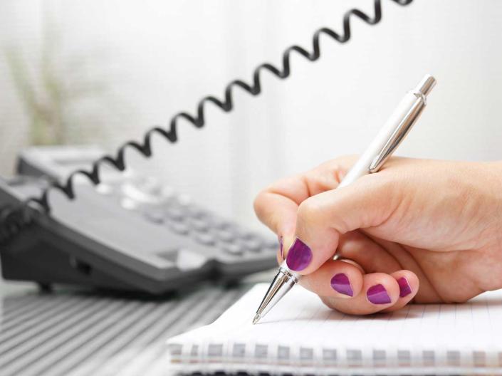 Person using a telephone and taking notes.