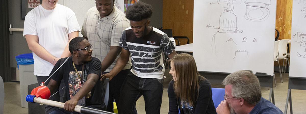 A group of students sit together testing out a mechanism