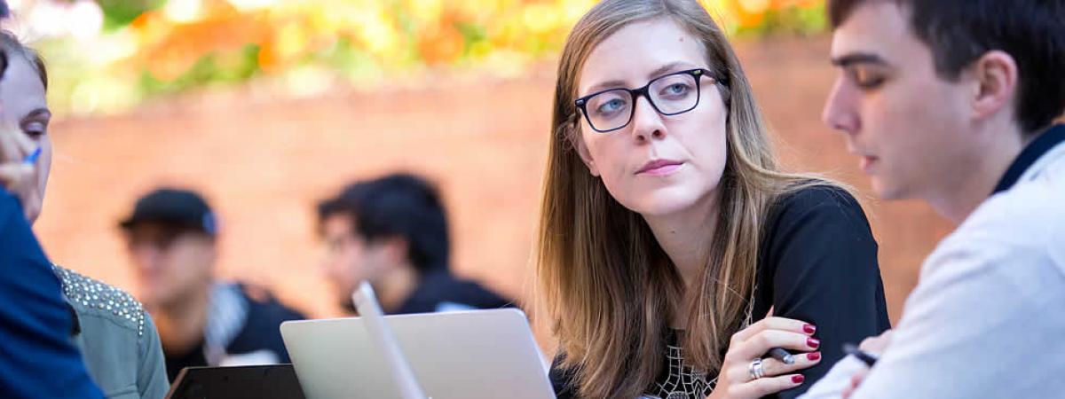 two law students studying outside with a laptop, with other students in background