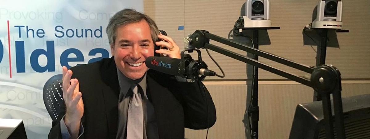 CWRU Co-Dean and Law Professor Michael Scharf, hosting Talking Foreign Policy radio program in recording booth, with the sound of ideas banner behind
