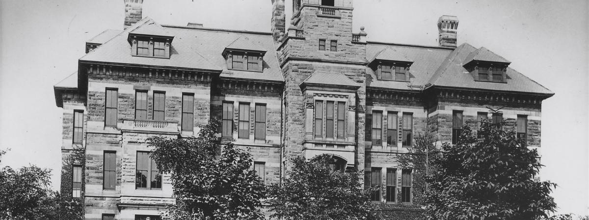 black and white exterior front view of 1 side of a building / grass lawn, trees, shrubs and sidewalk in foreground