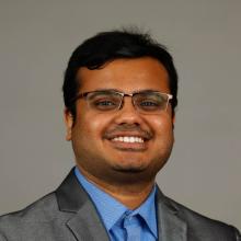 Headshot of Gourav Datta. He has short brown hair and glasses. He is wearing a grey suit and blue shirt.