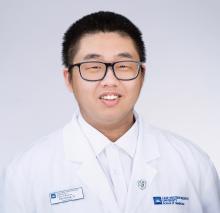 Man with glasses and dark hair wearing a white doctors coat
