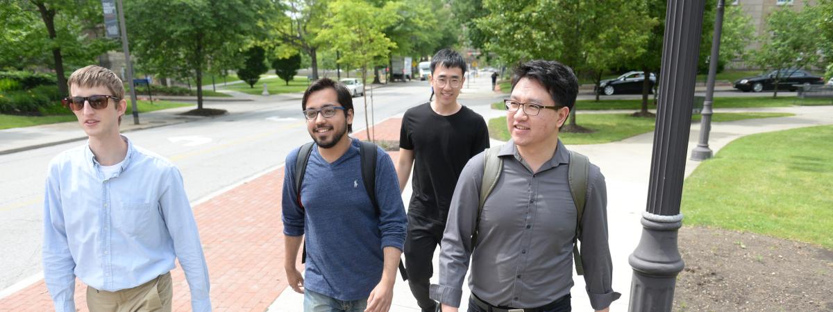 Four students walk down a sidewalk on a sunny day.