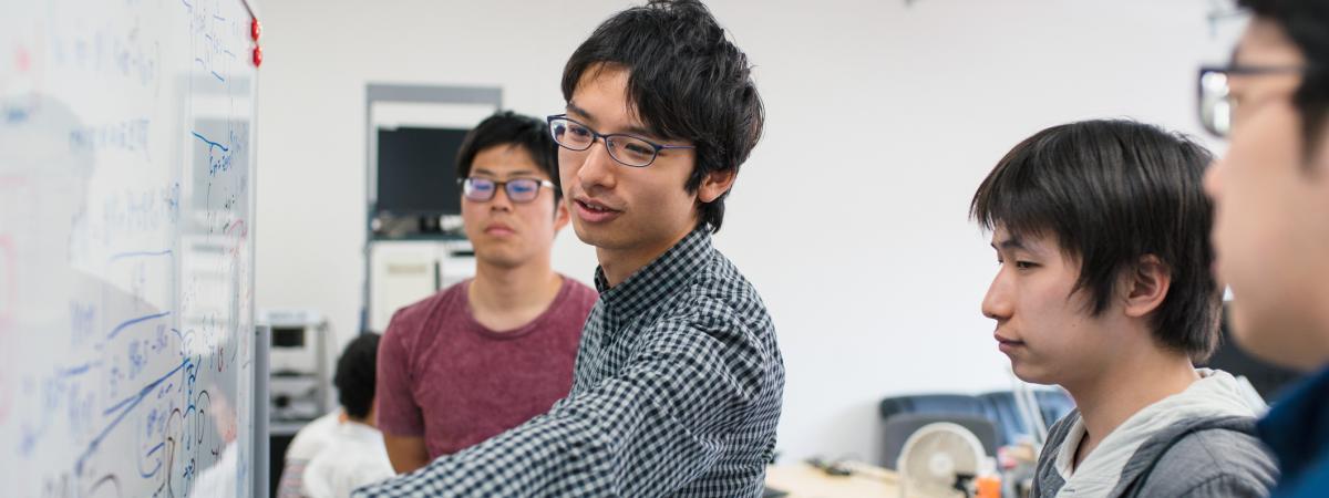 Small group of students looking at calculations on a white board