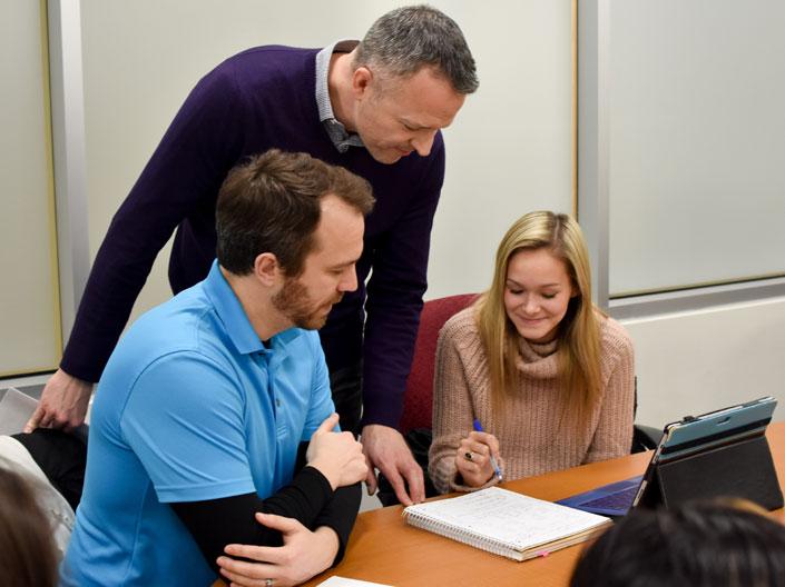 Instructor at Case Western Reserve University standing beside two seated students in a classroom