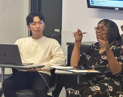 One student looks on as another talks to the class