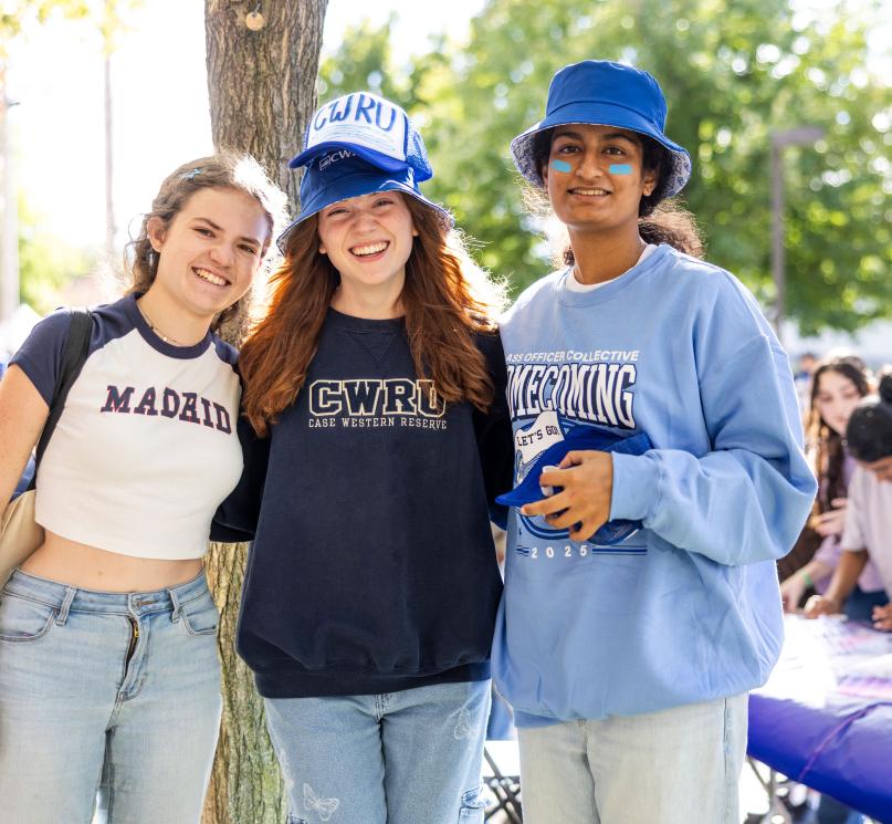 A group of three students in CWRU apparel pose outside smiling during homecoming.