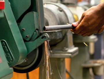 Close-up of a person using a green bench grinder with sparks flying.