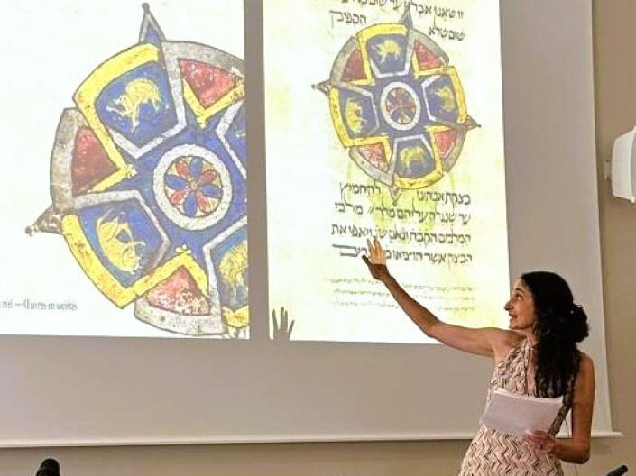 Photo of Elina Gertsman presenting at a symposium with the cover of her book on abstraction in medieval art projecting on the wall
