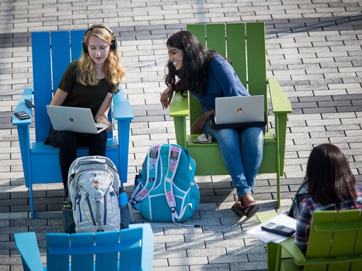 Two female CWRU students sitting in chairs looking at their computers