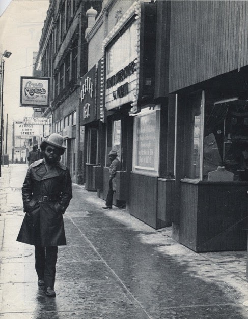 Winston Willis walking down Euclid in a long coat, hat and sunglasses