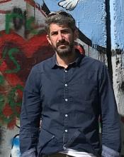 Photograph of Avidan Cover in front of the Israel-Palestinian border wall with grafitti