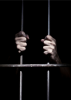 Photograph of hands grasping prison cell bars