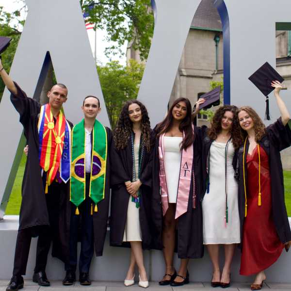 A group of six students posing with their arms in the air in front of a CWRU sign on campus.