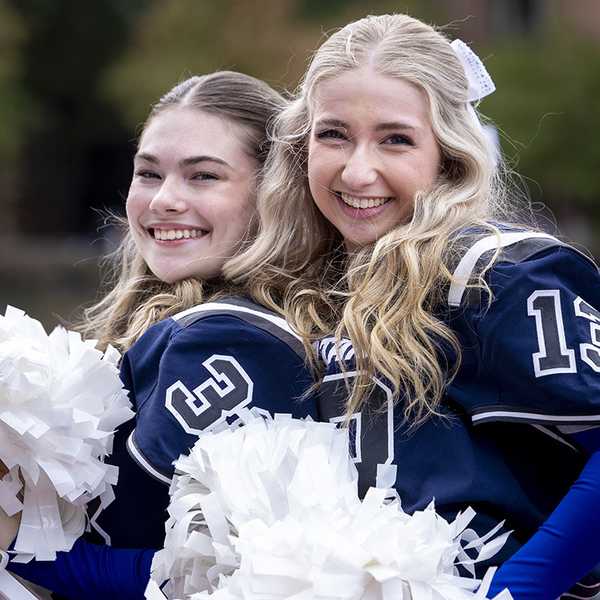 Two CWRU cheerleaders smiling and posing for a photo at the homecoming football game.