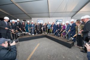 A group of people holding shovels and wearing hardhats dig into an arrow-shaped container of soil.