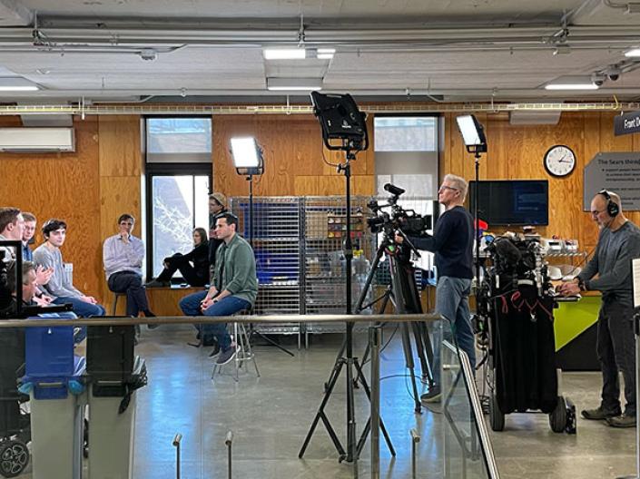 Multiple students sitting in front of a media team with cameras and lights