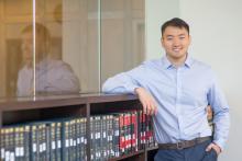 Jim Jiang leans against a library shelf while wearing a collared shirt