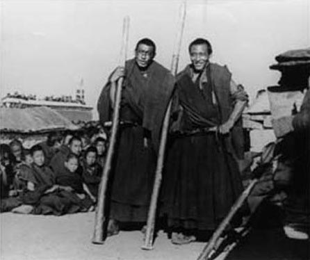 Black and white photograph of two smiling men in robes holding large wooden rods