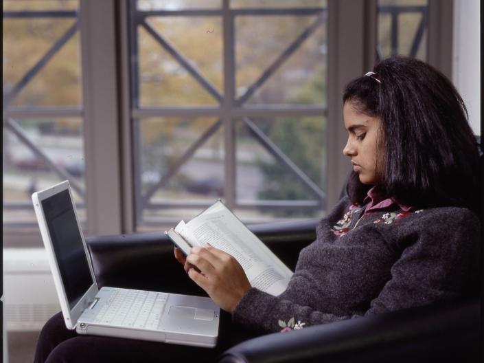 woman sitting with a book and laptop studying