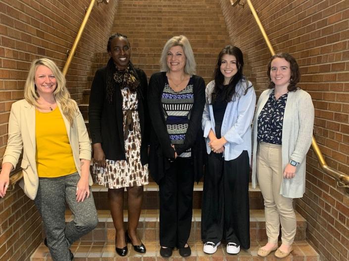 Group of five women posing on stairs against a brick wall.