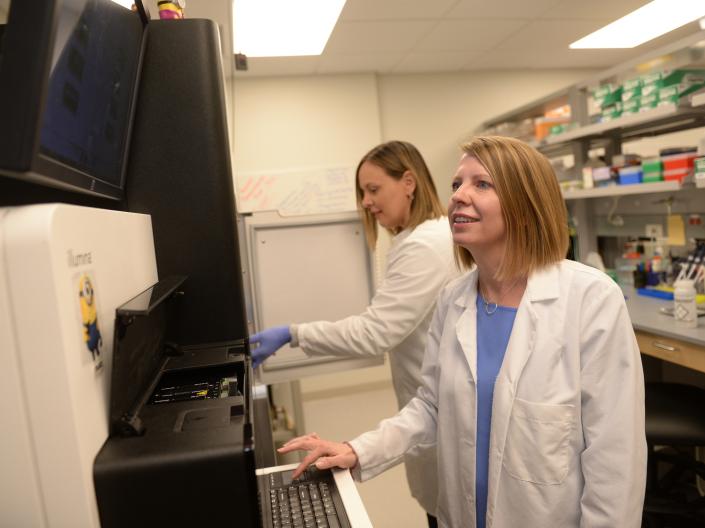 Two women wearing white lab coats work side by side using laboratory instruments.