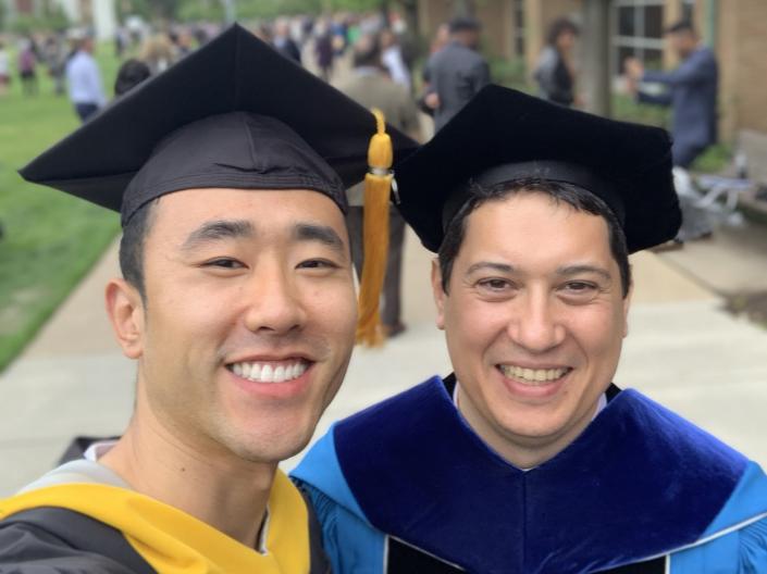 Two smiling men wearing graduation regalia.