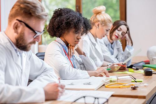 four medical students in white coats reading