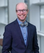 smiling man with glasses, bowtie, and dark suit