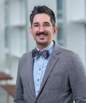 smiling man with glasses, bowtie, and gray suit