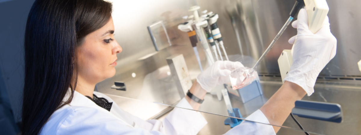 A lab technician using a syringe to put contents into a vial