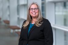 smiling woman with long hair and dark suit and glasses