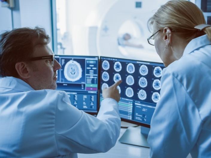 Two scientists in lab coats looking at brain scans