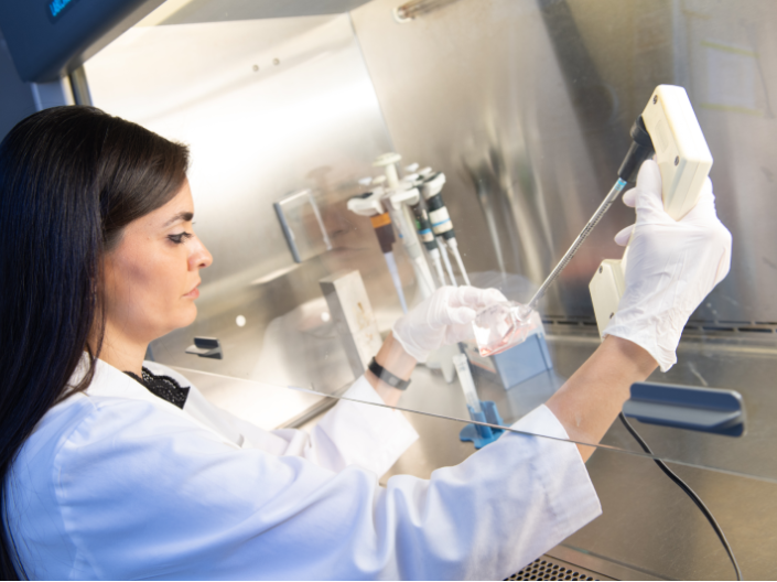 A lab technician using a syringe to put contents into a vial