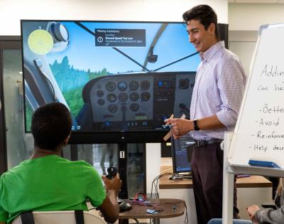 Photo of a PhD leading a demonstration of an aviation haptics program for a high school student