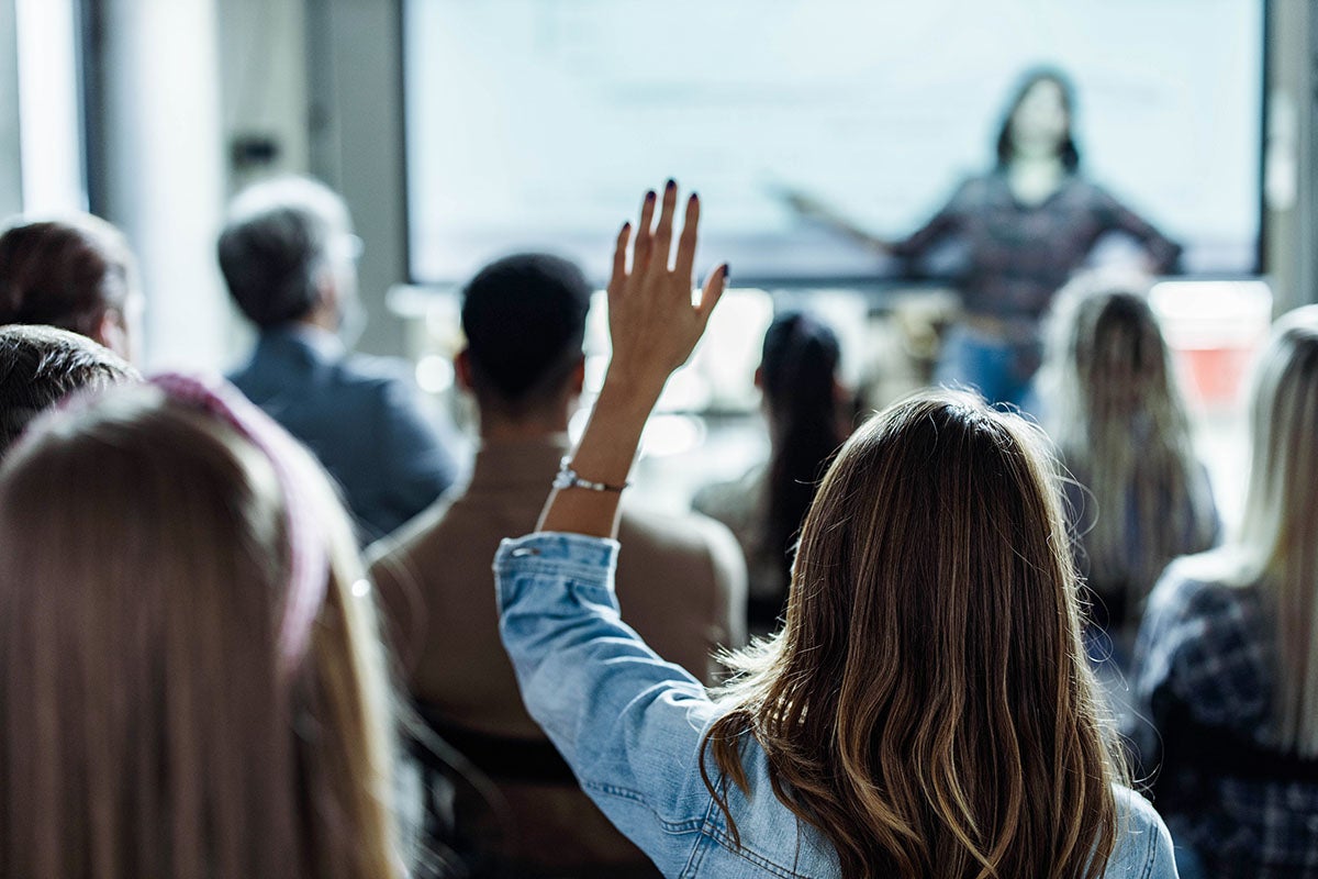 Women sitting in a seminar with her hand raised