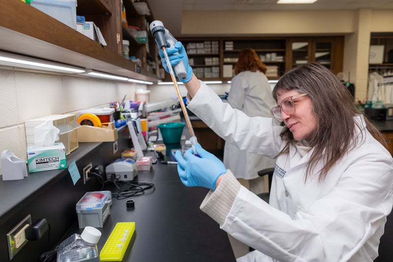 Person with a lab glasses and transferring liquid to beaker