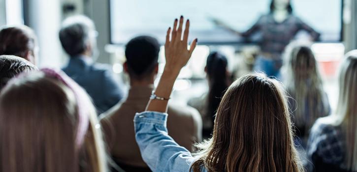 Women sitting in a seminar with her hand raised