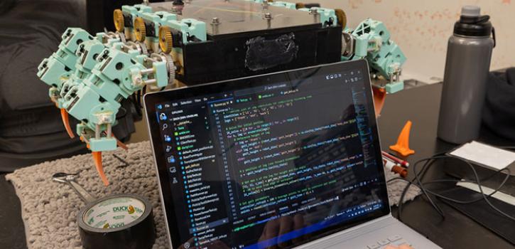 laptop computer with code on screen in front of a mechanical prototype