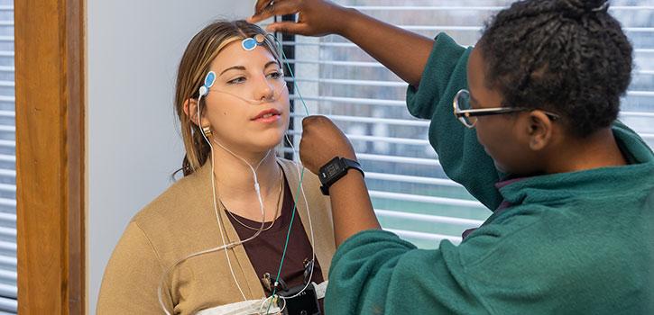 Two people one holding electrodes the other person's head.