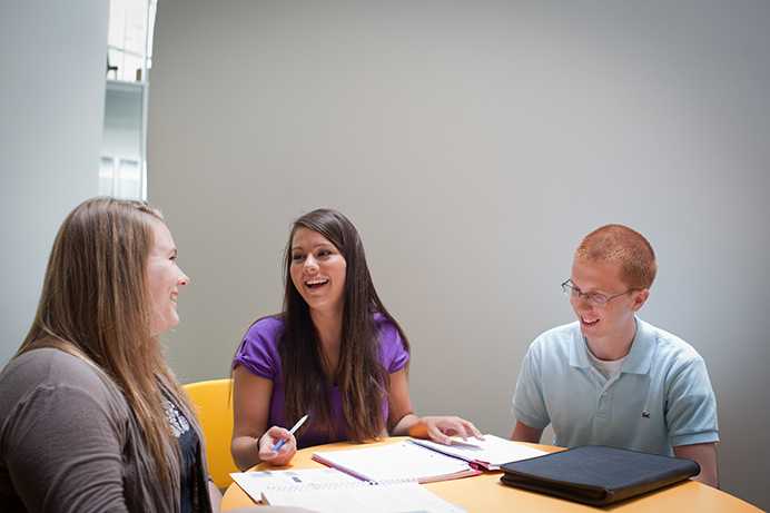 Three students sitting at a table laughing 