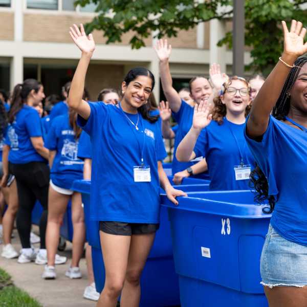 Students wave to incoming students next to blue move-in bins.